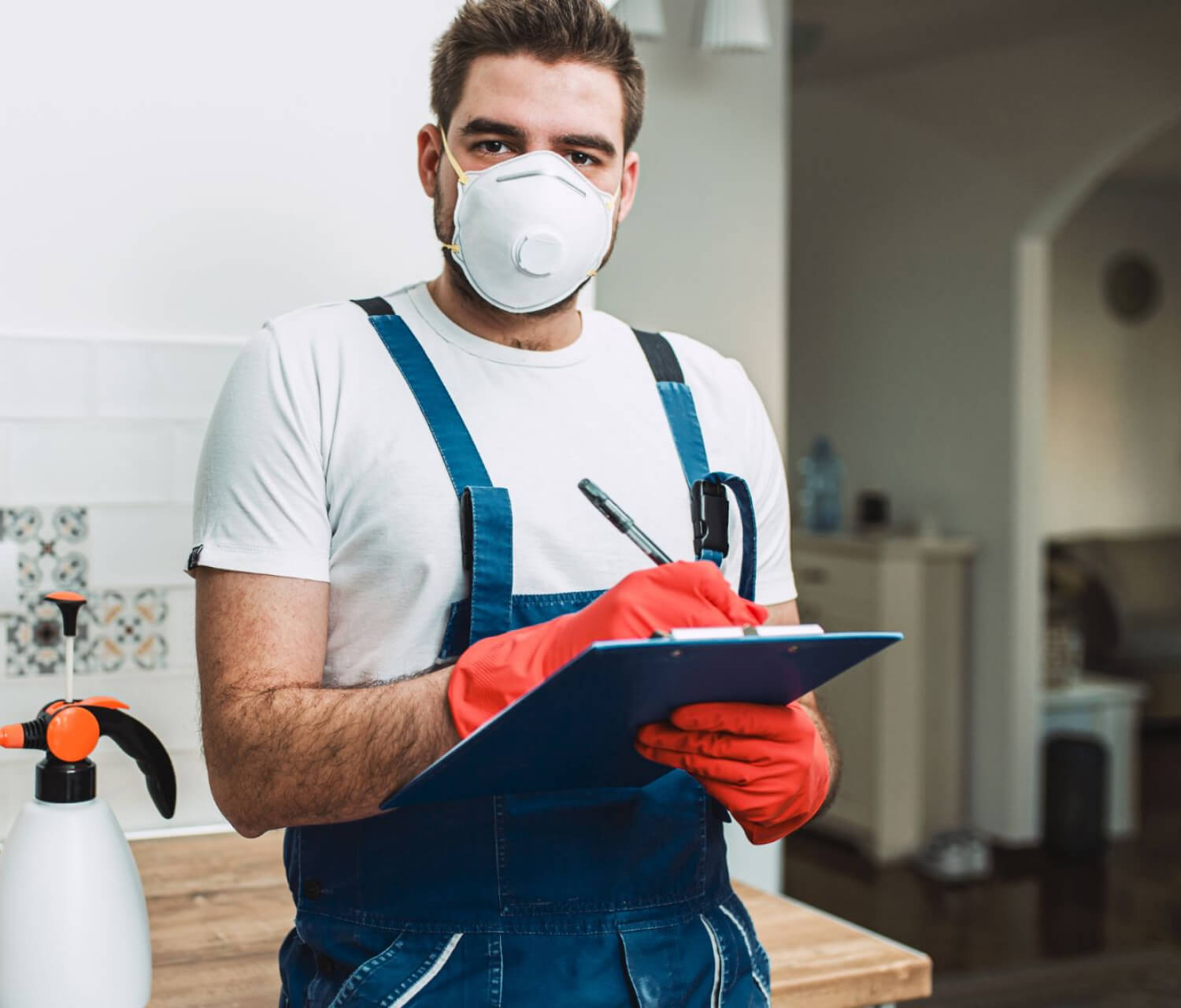 A termite specialist wearing a mask and gloves is holding a clipboard.